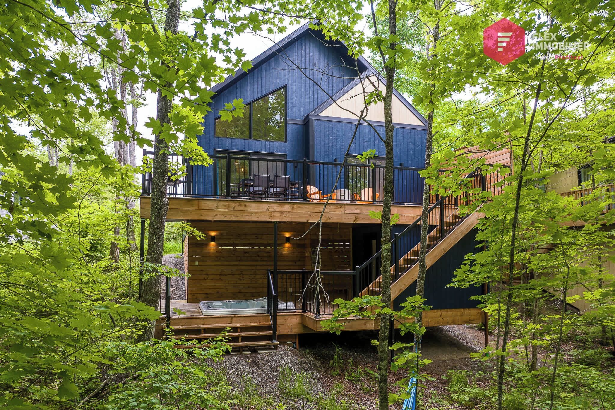 A two-story wooden cabin with a balcony, surrounded by trees.