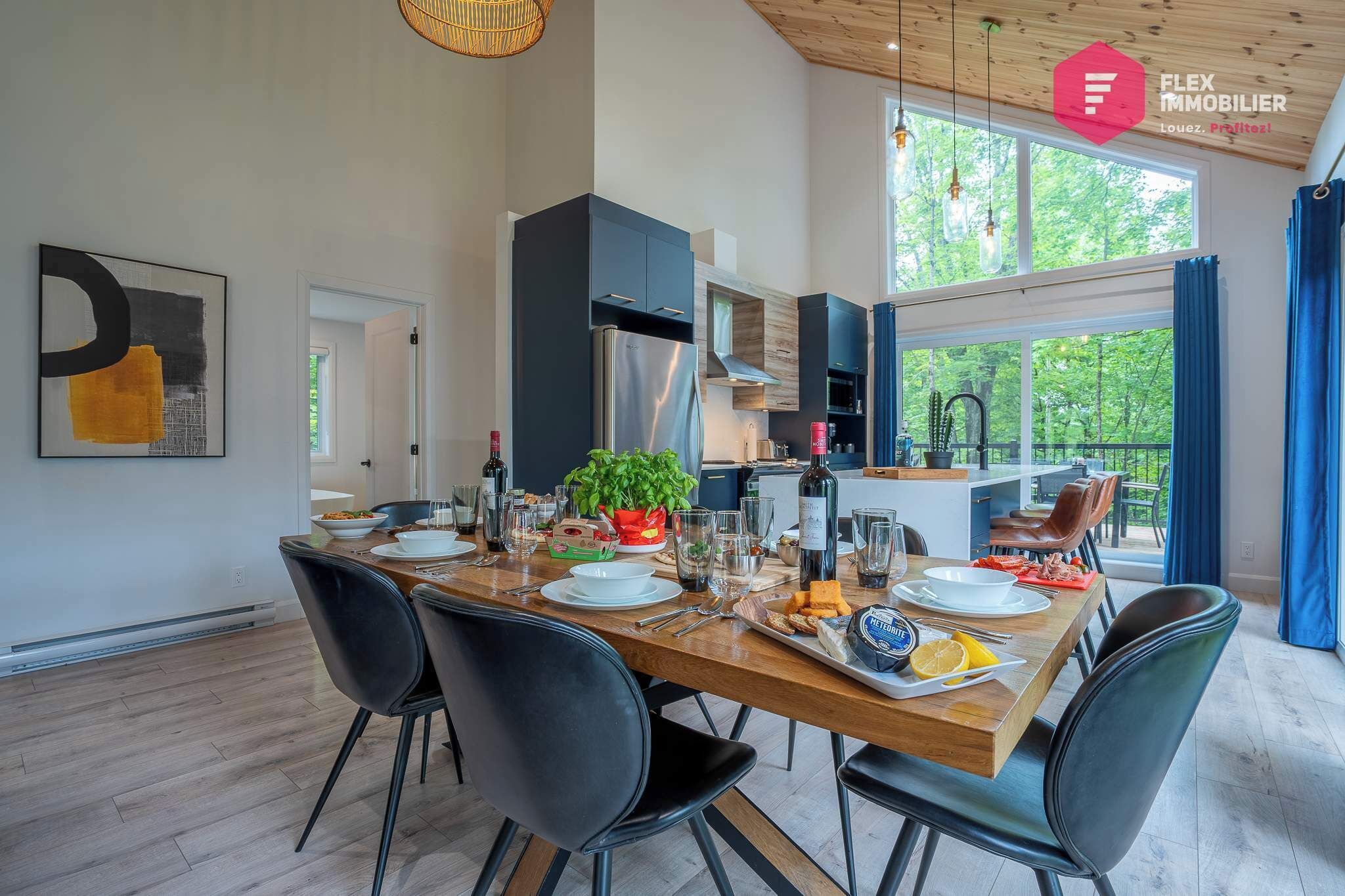 A modern dining area with a wooden table set for four, black chairs, and a kitchen in the background.