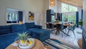 A modern living room with a blue sofa, dining area with chairs, and a kitchen in the background. - The Bellevue in Portneuf - Private SPA, 65-inch TV (Pont-Rouge)