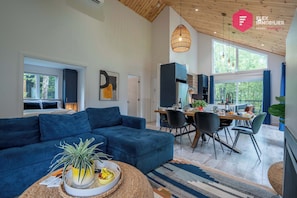 Ein modernes Wohnzimmer mit einem blauen Sofa, einem Essbereich mit Stühlen und einer dahinterliegenden Küche.