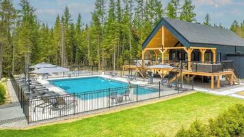 A cabin with a pool, surrounded by a wooden deck and a fenced area with lounge chairs.