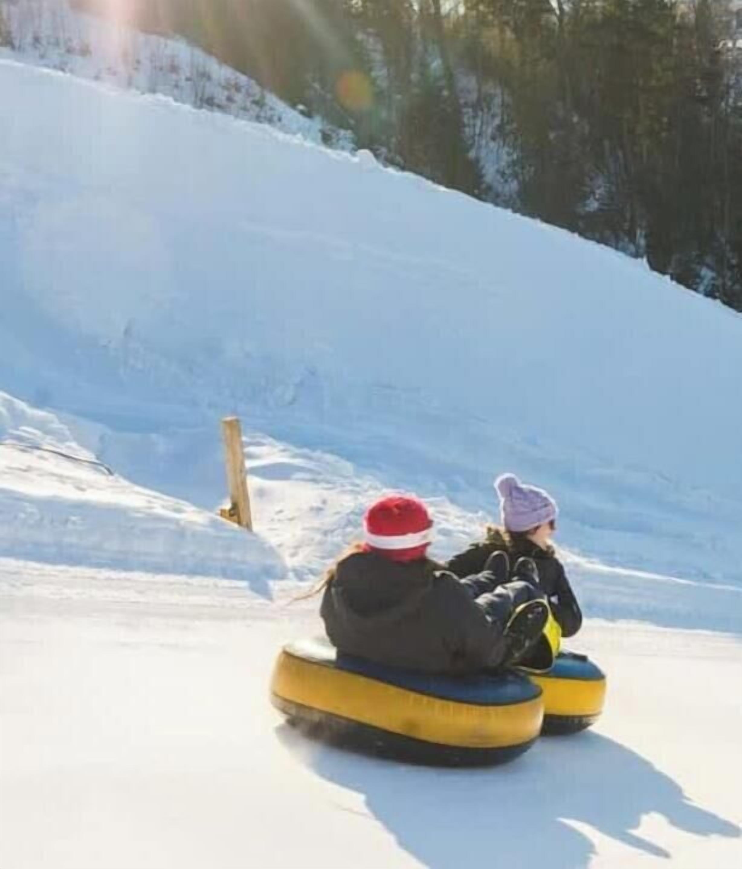 Two people on snow tubes on a snowy slope.