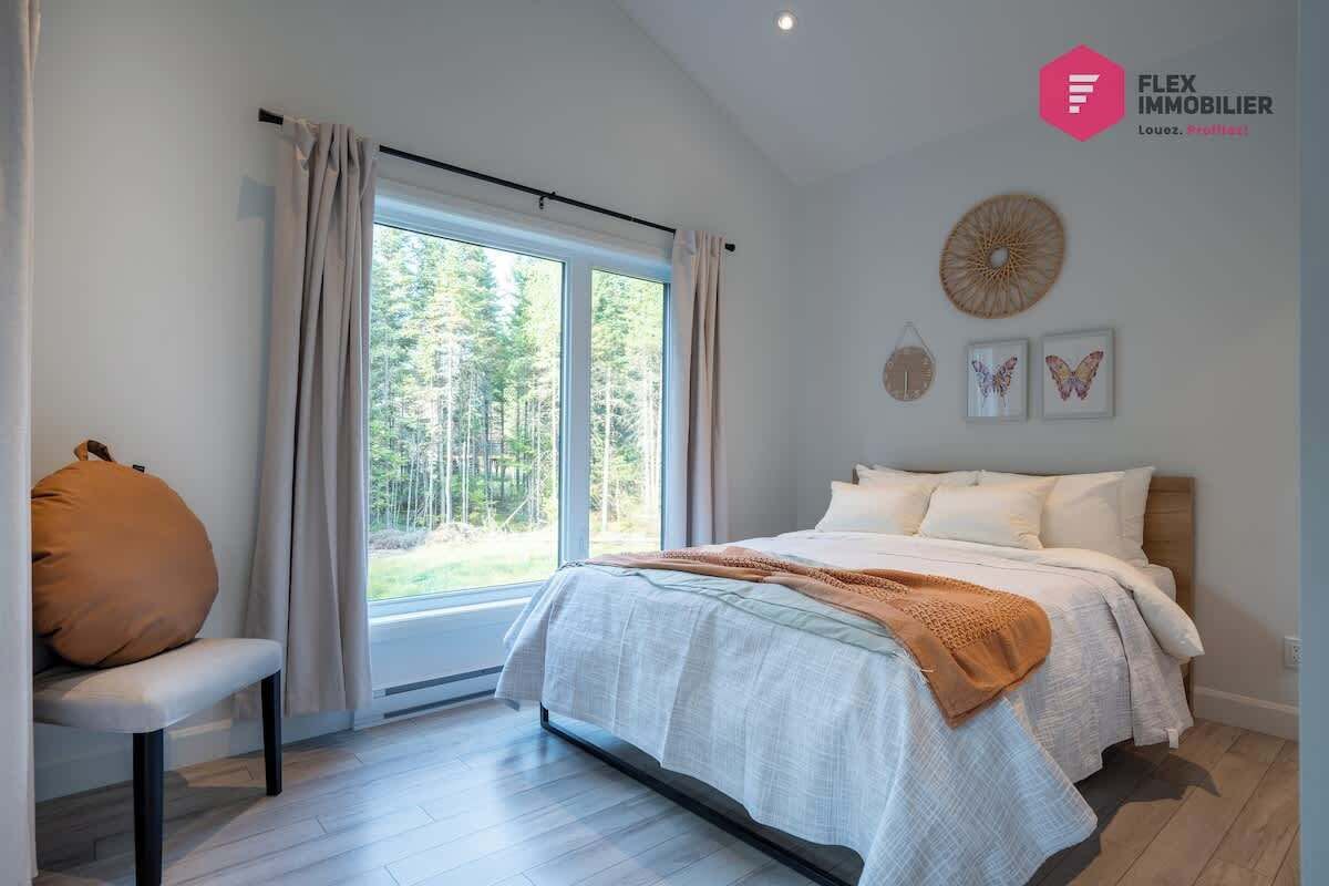 Une chambre avec une grande fenêtre, un lit avec une literie blanche, un banc avec un coussin et un mur décoré de différents objets.