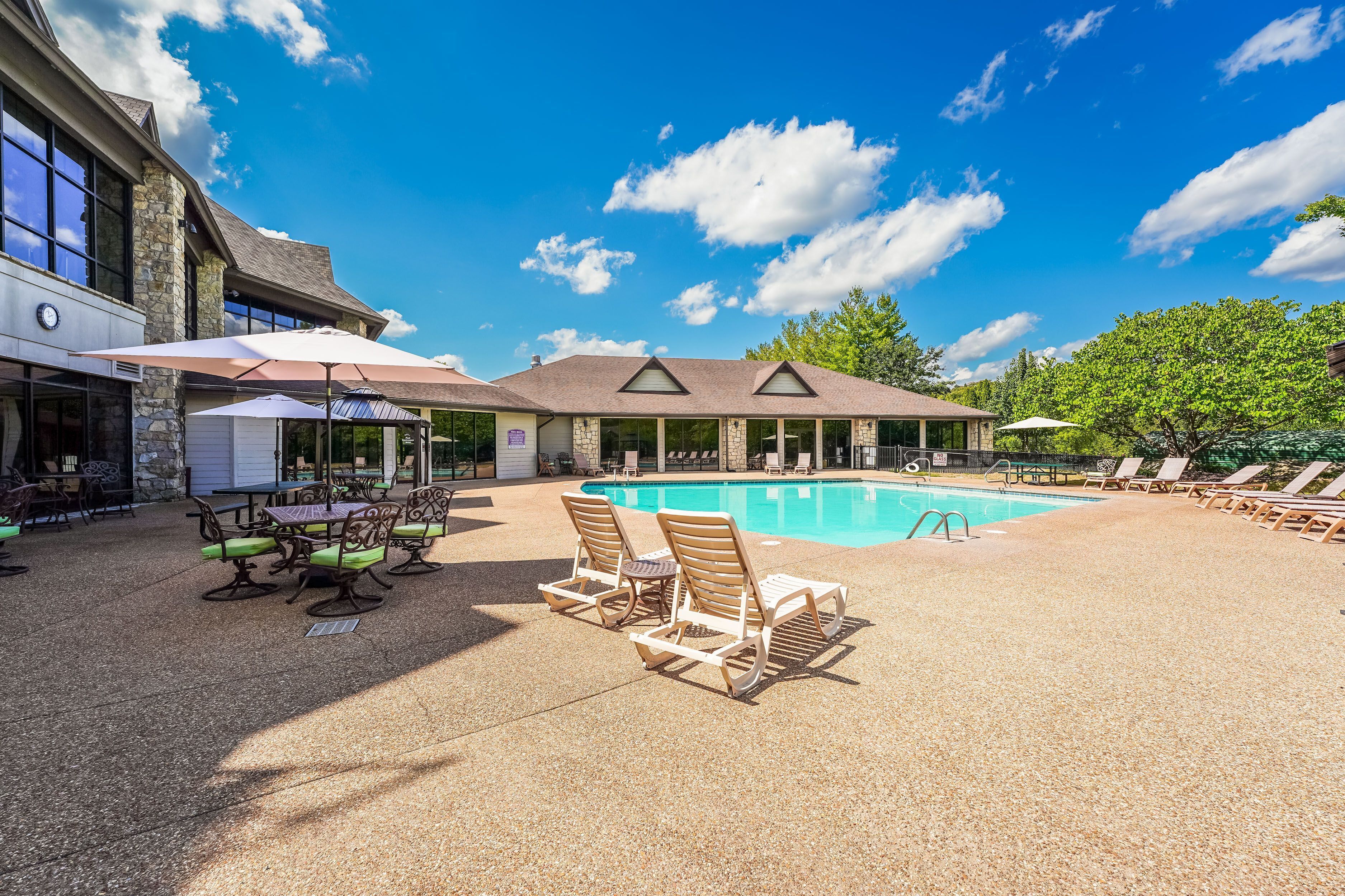 Een zwembadgedeelte met ligbedden, een tafel met parasols en een gebouw met grote ramen.