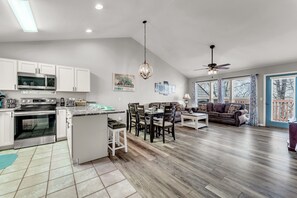 A modern kitchen with white cabinets, a central island, and a dining area with a table and chairs. - Peaceful Stonebridge Condo w/ Resort Amenities (Branson West)