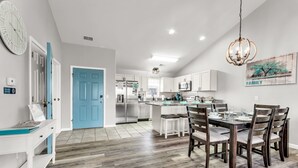 Una cocina moderna con armarios blancos, una puerta azul y un comedor con sillas de madera y una mesa.