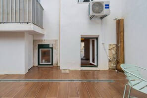 Un patio con piso de baldosas, una silla de metal, una puerta de madera y un equipo de aire acondicionado.