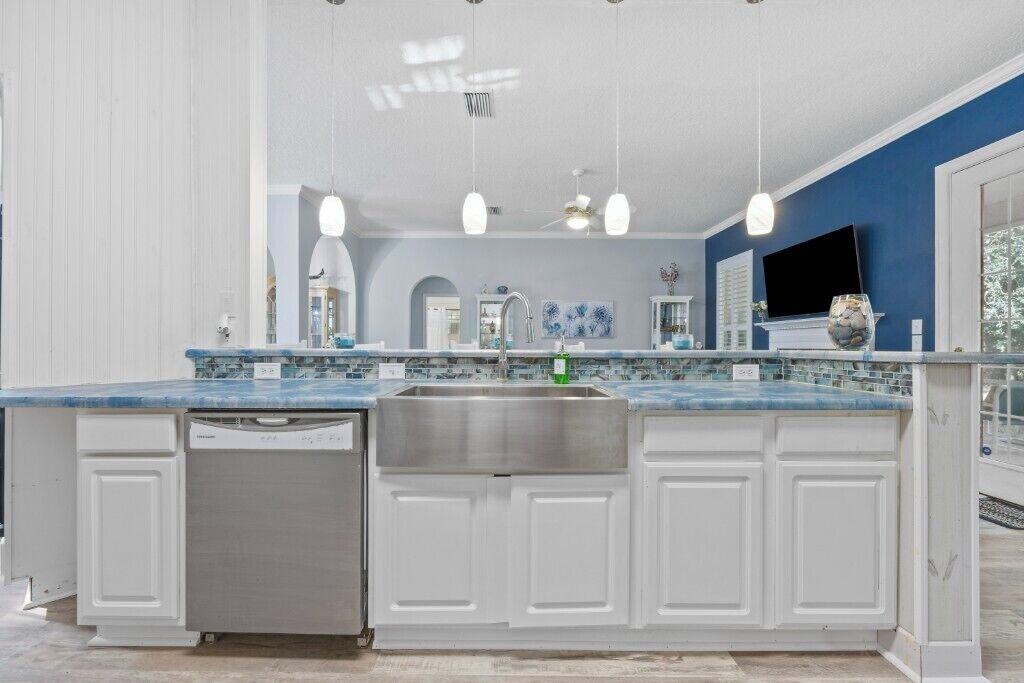 A kitchen with a large island, white cabinetry, a stainless steel sink, and pendant lighting.