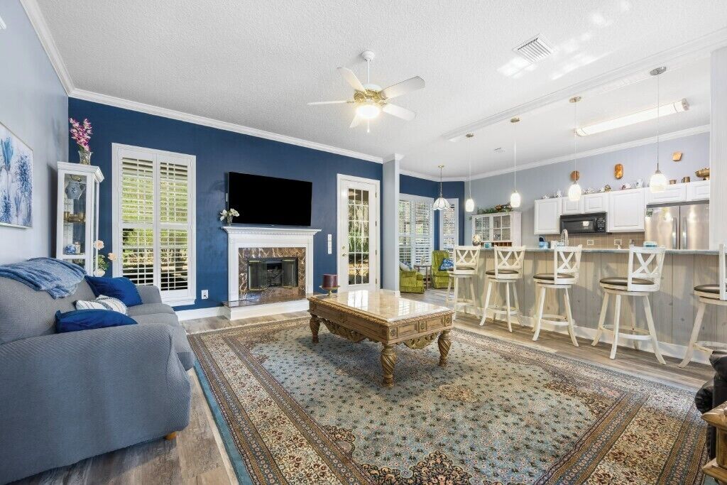A living room with a sofa, a coffee table, and a fireplace. There is a kitchen area with bar stools and a television.