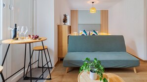 A compact room with a green sofa, a small wooden table with a potted plant, and a tall lamp. - Cozy House B - By Y Concept (Setúbal)