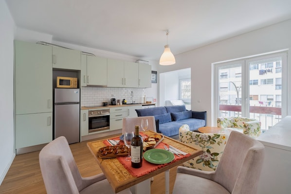 A modern kitchen with a dining area, a sofa, and a view of the outside.