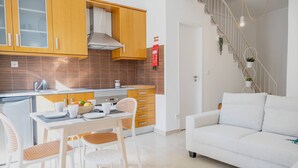 A modern kitchen with wooden cabinets, a dining area with white chairs, and a staircase leading to a living area with a white sofa. - Setubal Downtown - By Y Concept (Setúbal)