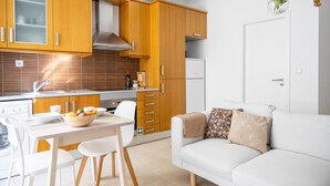 A modern kitchen with wooden cabinets, a white countertop, and a dining area with a table and chairs. - Setubal Downtown - By Y Concept (Setúbal)