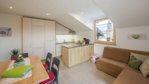 Un espacio habitable compacto con kitchenette, comedor y zona de estar con sofá y mesa.