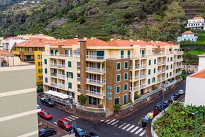 Un immeuble résidentiel à plusieurs étages, doté de balcons, donnant sur une rue et ayant une colline en arrière-plan.