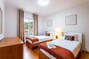 Une chambre d’hôtel avec deux lits, un bureau en bois, une fenêtre avec des rideaux et un tableau encadré au mur.