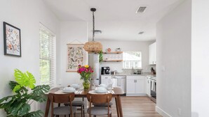 A dining area with a table set for four, a hanging light fixture, and a kitchen in the background. - Serene Place, Walk to UF, Stadium, Near Shands & Downtown (Gainesville)