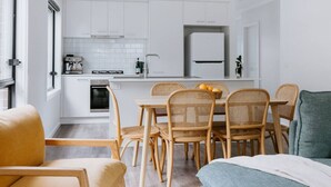 A modern kitchen with white cabinets, a built-in oven, and a coffee machine. There is a dining area with a table and wicker chairs. - 2 Houses, Sleeps 12, 4 Bathrooms, Private Location (Sale)