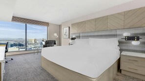 Habitación de hotel con una cama grande, un escritorio, una silla y vistas a un paisaje urbano.