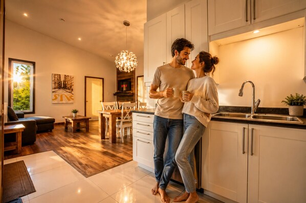 A modern kitchen with white cabinets, a stainless steel sink, and a dining area with wooden furniture. - Modern• Riverfront• Spa•firepit • 8 min Lac Simon (Chénéville)