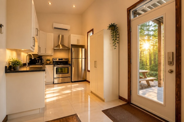Una cocina moderna con electrodomésticos de acero inoxidable, horno empotrado y un amplio ventanal con vistas a un bosque.