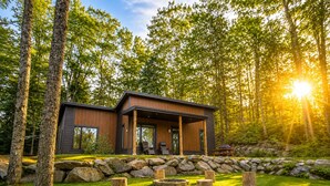 Une cabane moderne dotée d’un porche abrité, entourée d’un mur de pierres et d’une pelouse verdoyante.