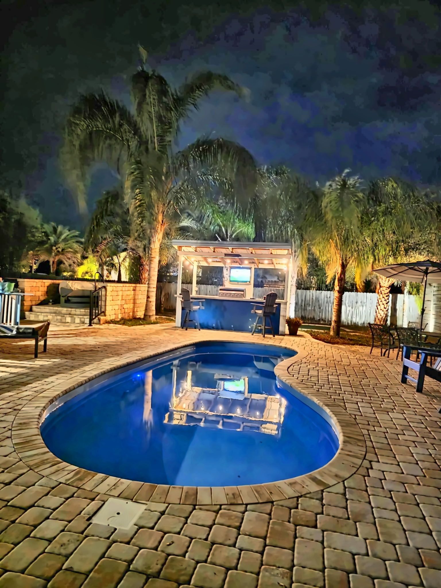 Une piscine dotée d’un jacuzzi intégré, entourée d’une terrasse en briques et de palmiers.