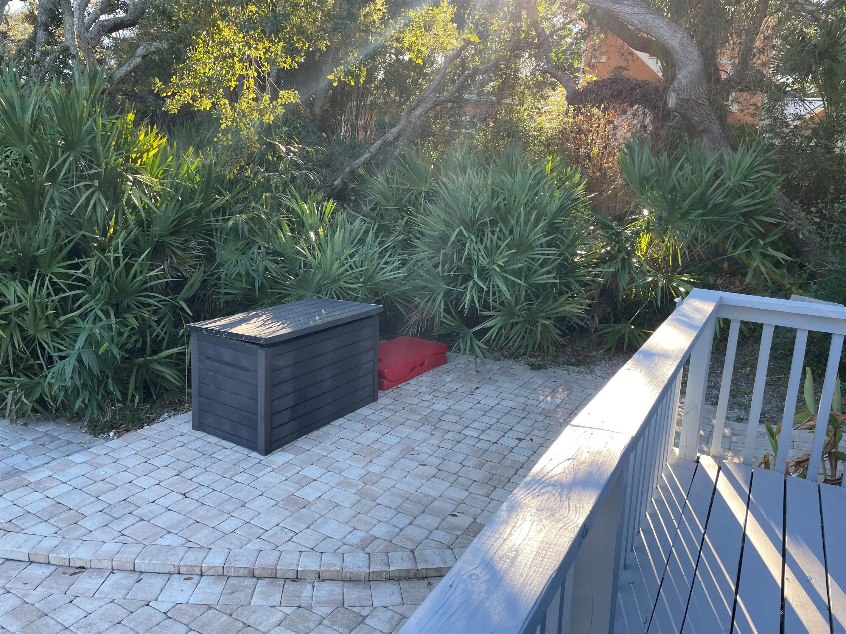 Zona d'un pati pavimentat amb una caixa de plegar de color fosc i un objecte vermell a terra.