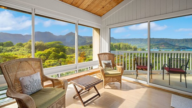 Een balkon met rieten stoelen, een houten tafel en uitzicht op bergen en groen.