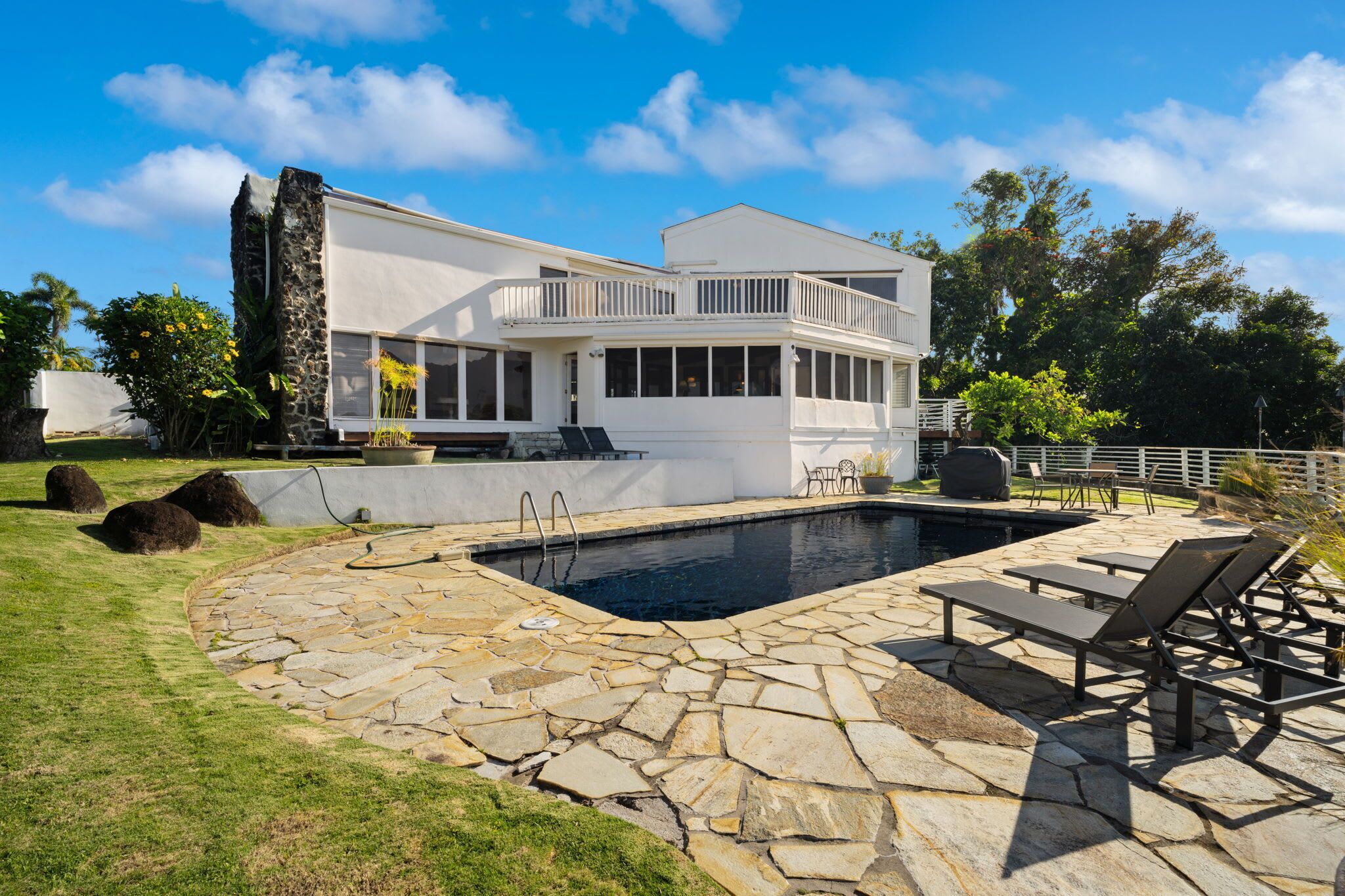 Una casa moderna con piscina, patio de piedra y mobiliario exterior.