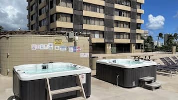 A hotel with two outdoor hot tubs, a stone wall with caution signs, and a multi-story building in the background.