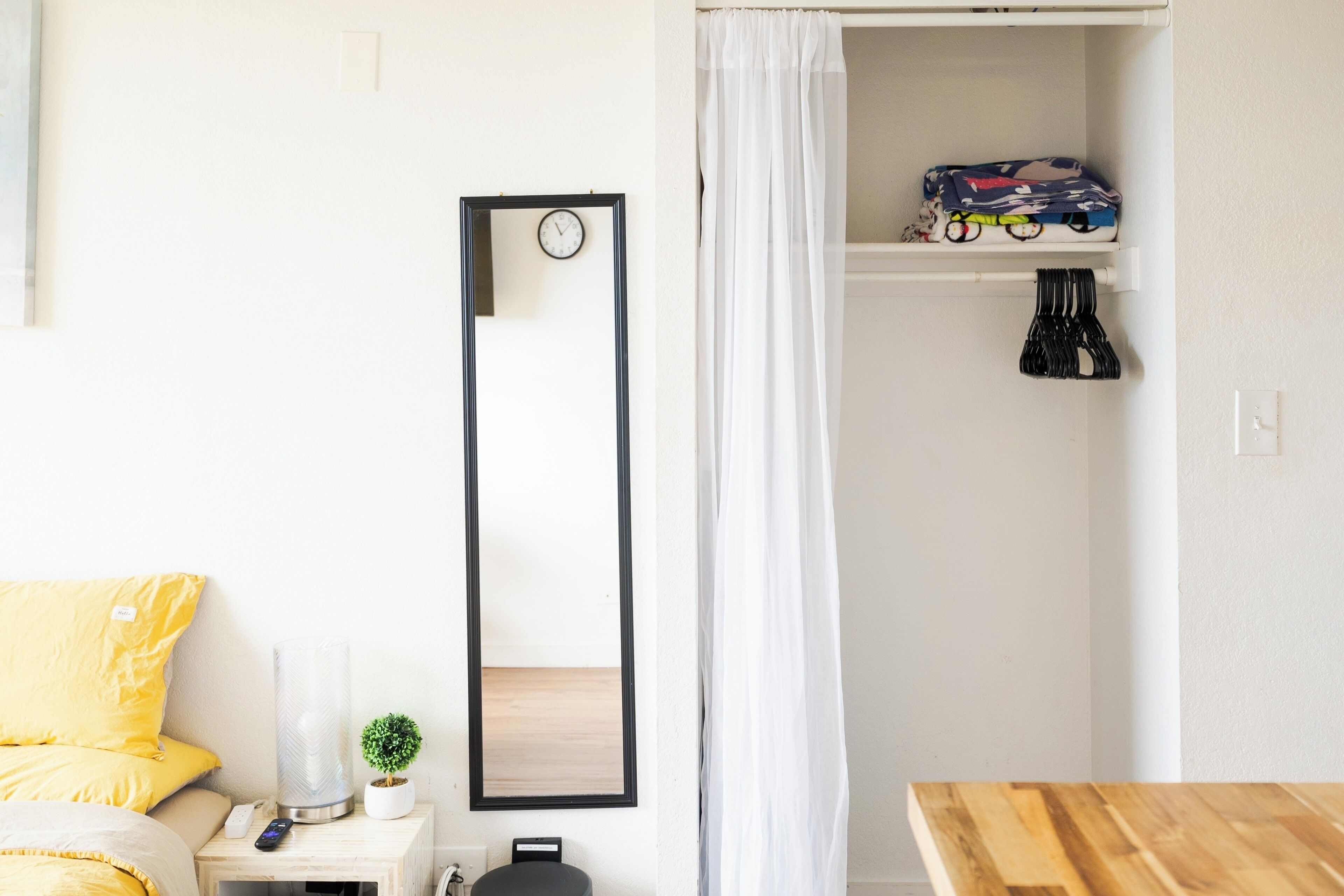 A bedroom with a bed, bedside table, mirror, and a shelf with folded clothes.