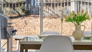A dining area with a table set for two, a white pitcher with flowers, and a view of a brick building and a wooden fence. - City-Close Durham Stay Near Downtown~Self Check-In~King Suite~Free Parking (Durham)