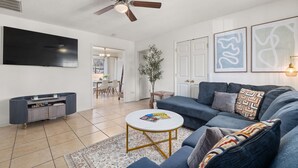 A modern living room with a large flat-screen TV, a blue sofa, a coffee table, and a ceiling fan. - City-Close Durham Stay Near Downtown~Self Check-In~King Suite~Free Parking (Durham)