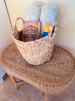 A wicker basket containing a bottle, a box, and two towels on a wicker chair.