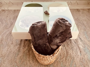 A pair of dark brown towels folded and placed in a woven basket on a white rectangular object with a glass top, set on a textured beige carpet.