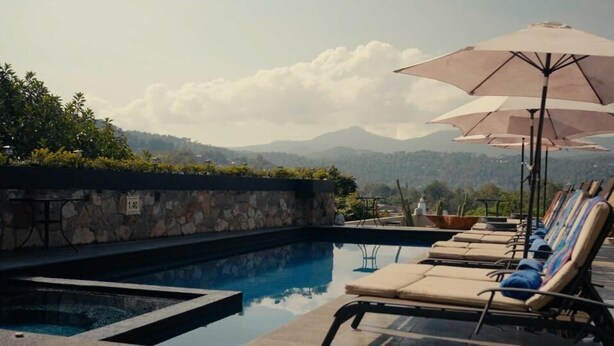 A pool area with lounge chairs and umbrellas, a stone wall, and a view of mountains. - EL SECRETO DE VALLE (Valle de Bravo)