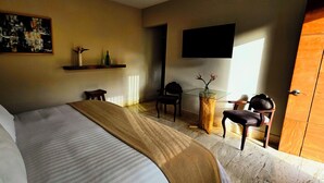 A hotel room with a bed, a TV mounted on the wall, a wooden door, and a small table with chairs. - EL SECRETO DE VALLE (Valle de Bravo)