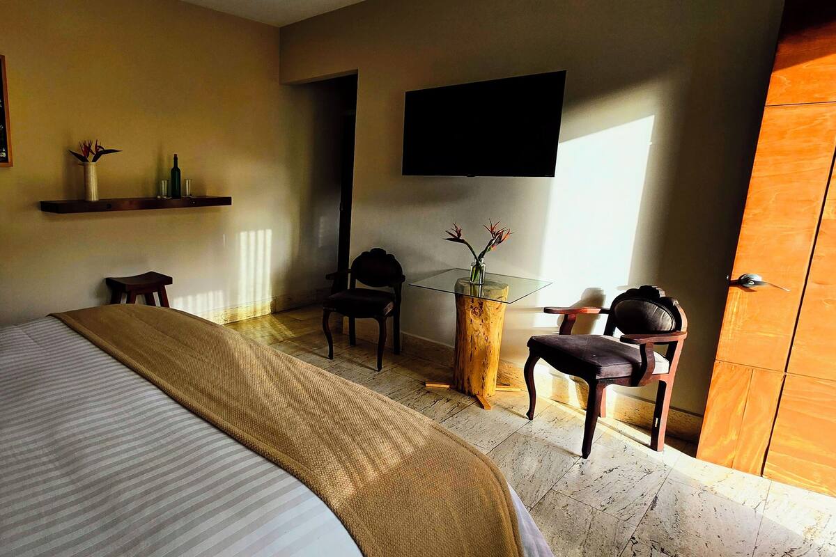 A hotel room with a bed, a TV mounted on the wall, a wooden door, and a small table with chairs.