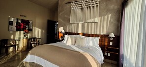 A hotel room with a large bed, a wooden headboard, a bedside table with a lamp, a small table with a vase of flowers, and a painting on the wall. - EL SECRETO DE VALLE (Valle de Bravo)