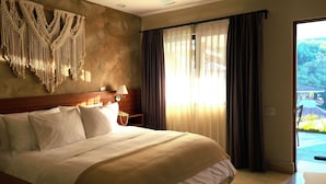 A hotel room with a large bed, a macrame wall hanging, a bedside table with a lamp, and a view of a garden through sheer curtains. - EL SECRETO DE VALLE (Valle de Bravo)