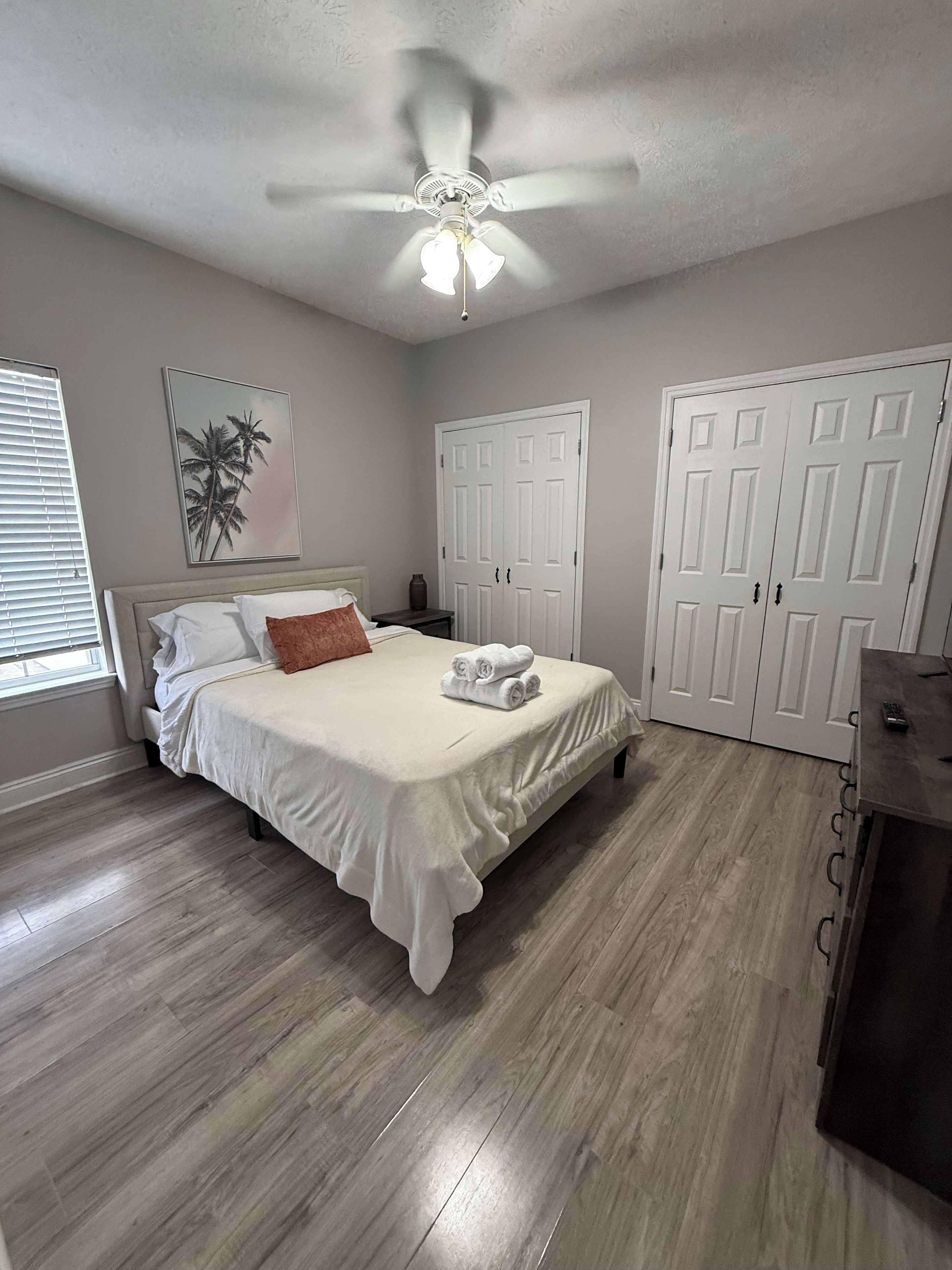 A bedroom with a bed, a ceiling fan, a nightstand, a dresser, and a door.