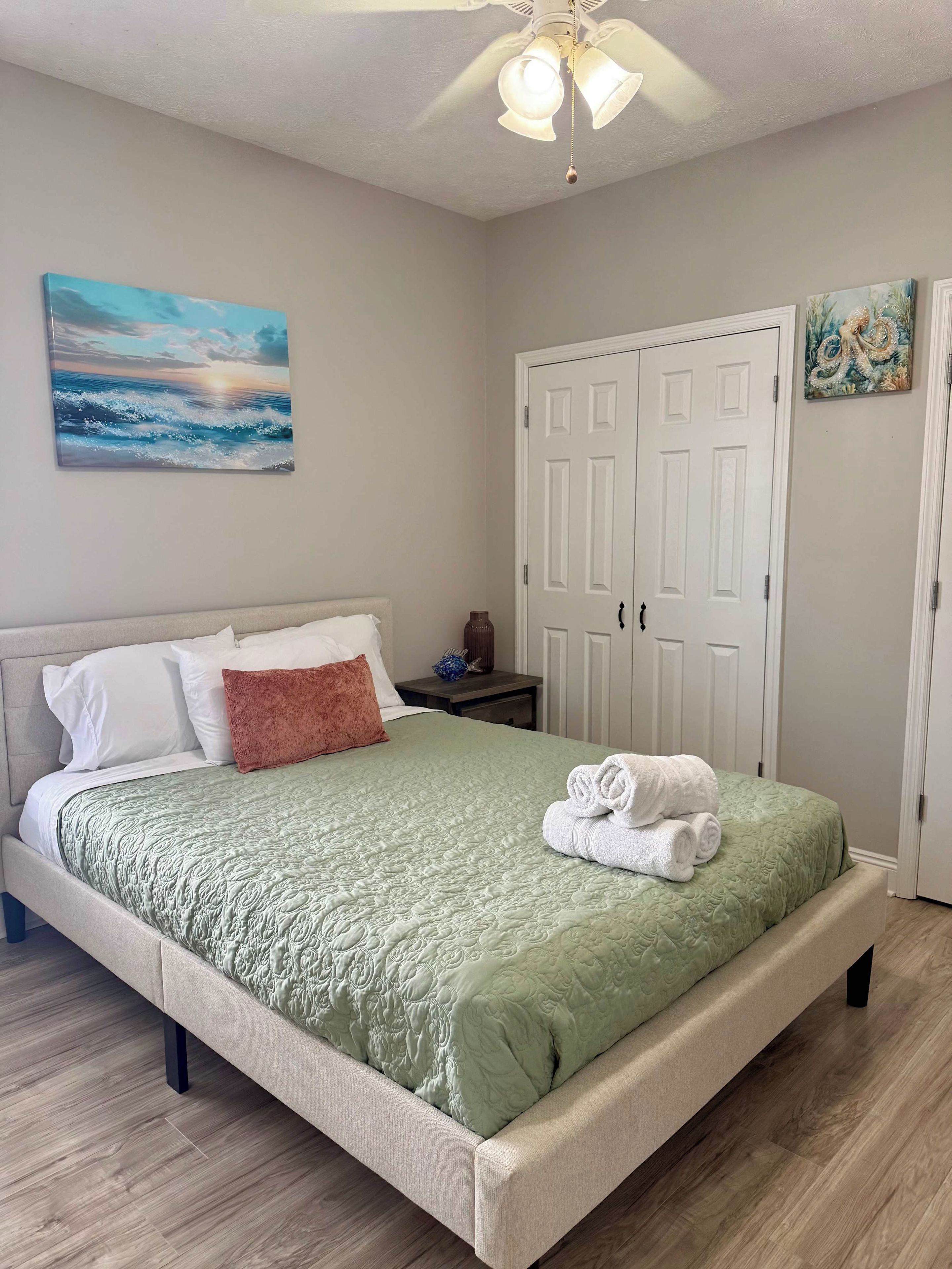 A bedroom with a bed, a nightstand, a painting, and a wardrobe.
