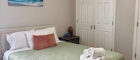 A bedroom with a bed, a nightstand, a painting, and a wardrobe.