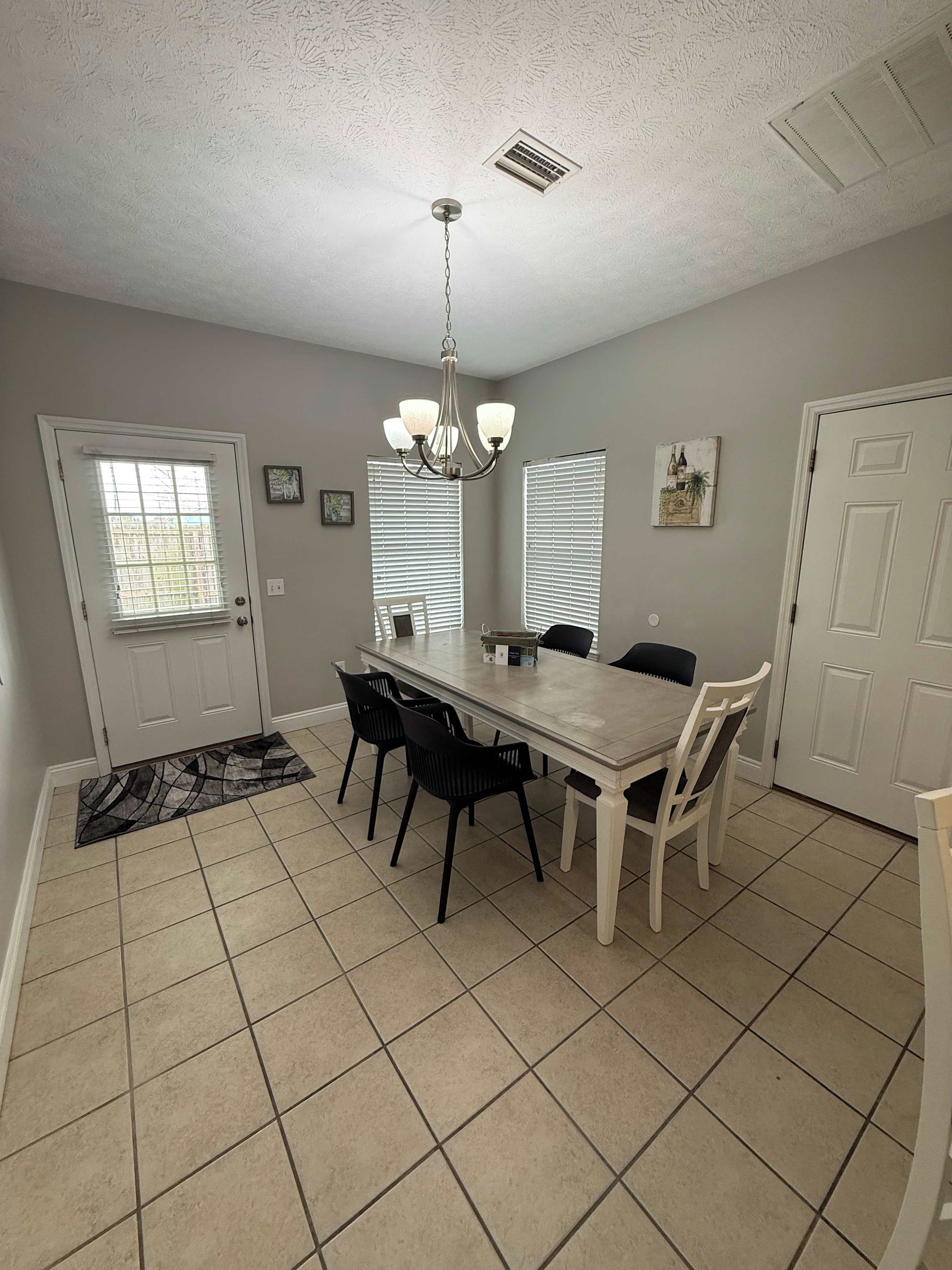 A dining area with a table, chairs, a chandelier, and a patterned rug.