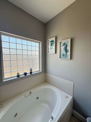 Een badkamer met een ruime badkuip, een matig doorzichtig raam en twee kunstwerken in lijsten aan de muur.