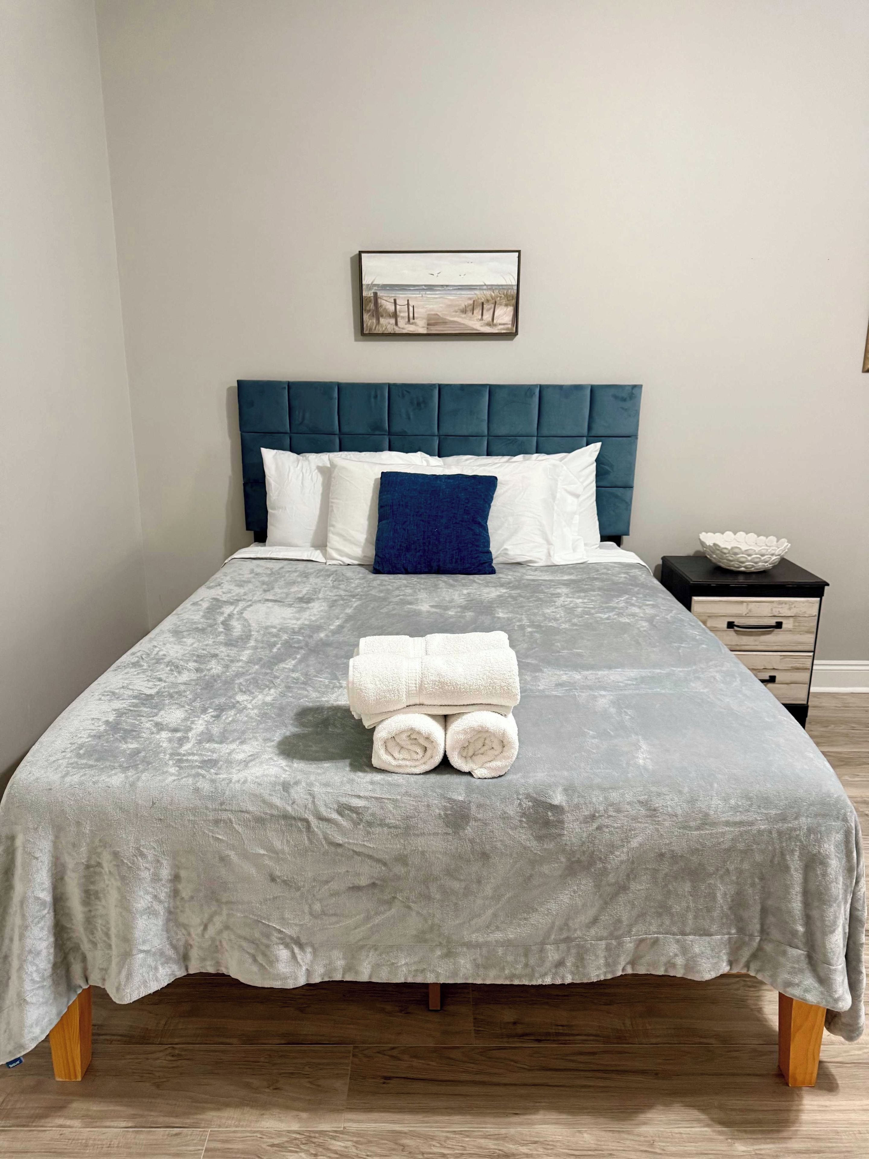 Un lit bien fait, avec une couverture grise à texture, une tête de lit bleue et un oreiller blanc.