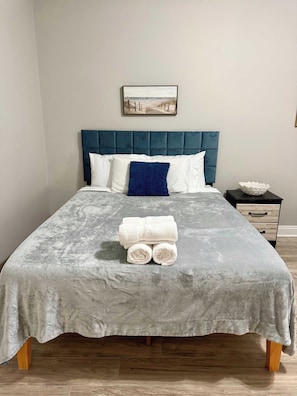 A neatly made bed with a grey textured bedspread, a blue headboard, and a white pillow. - Beach Days, Nightlife Nights, East End of PCB (Panama City)