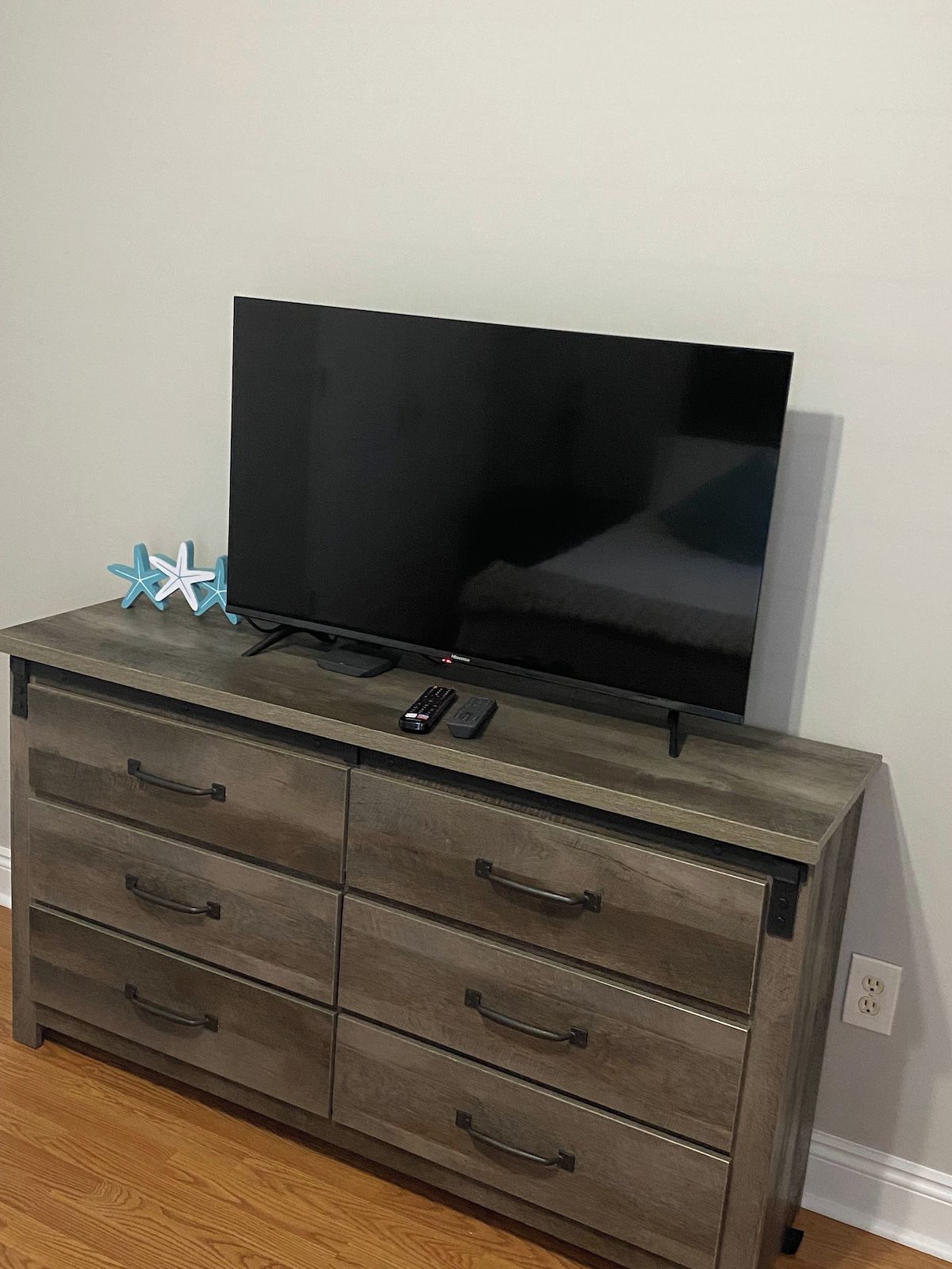 A television on a wooden dresser with drawers and a remote control.