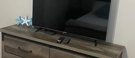 A television on a wooden dresser with drawers and a remote control.